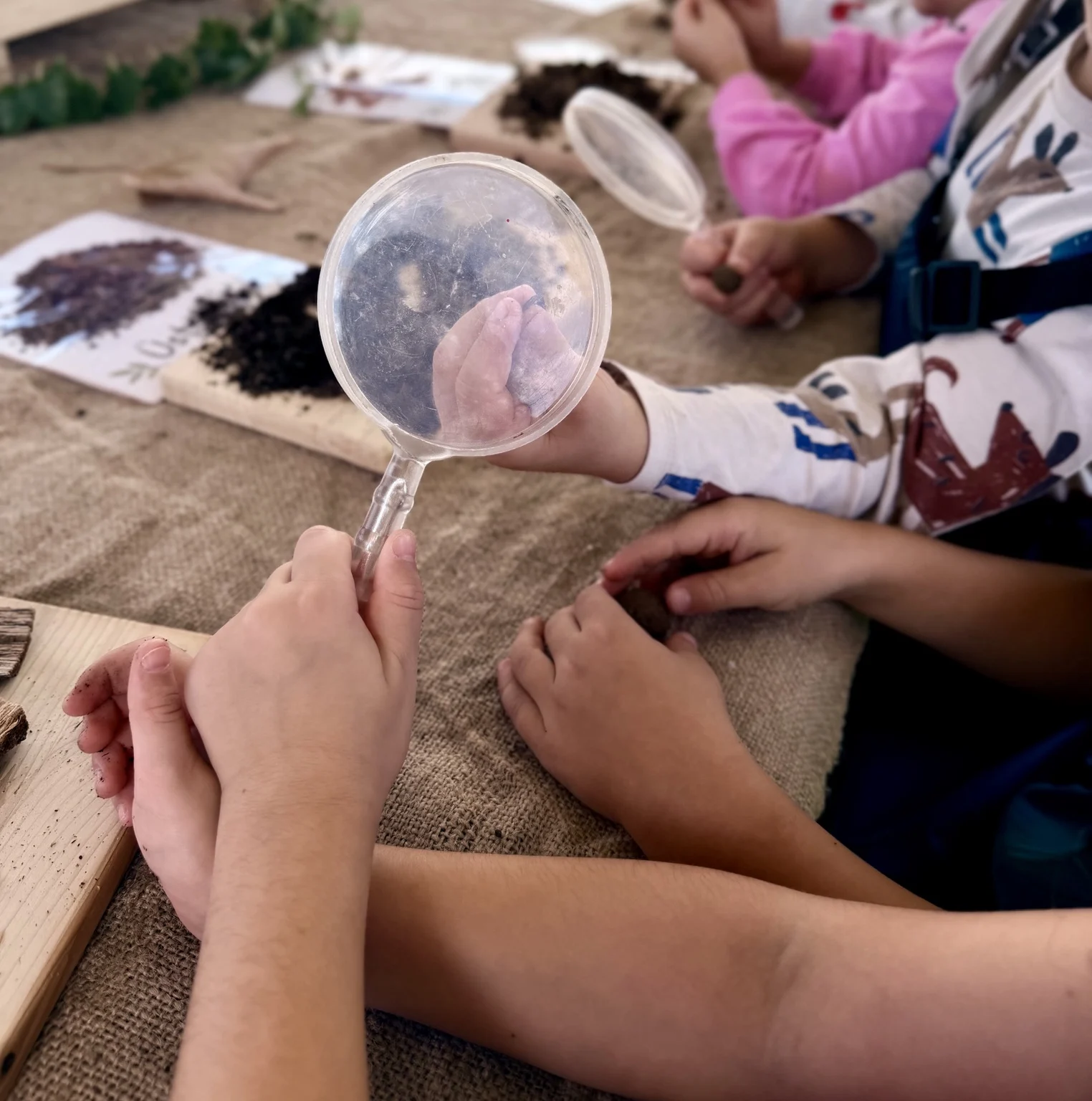 Büyüteçlerle doğal malzemeleri inceleyen çocukların elleri
